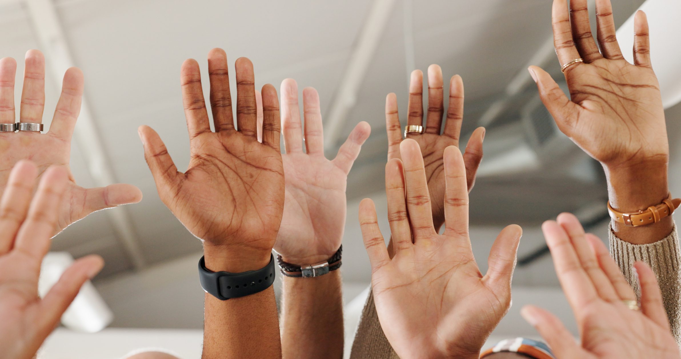 A group of diverse hands raised in the air, showing various skin tones and wrist accessories.